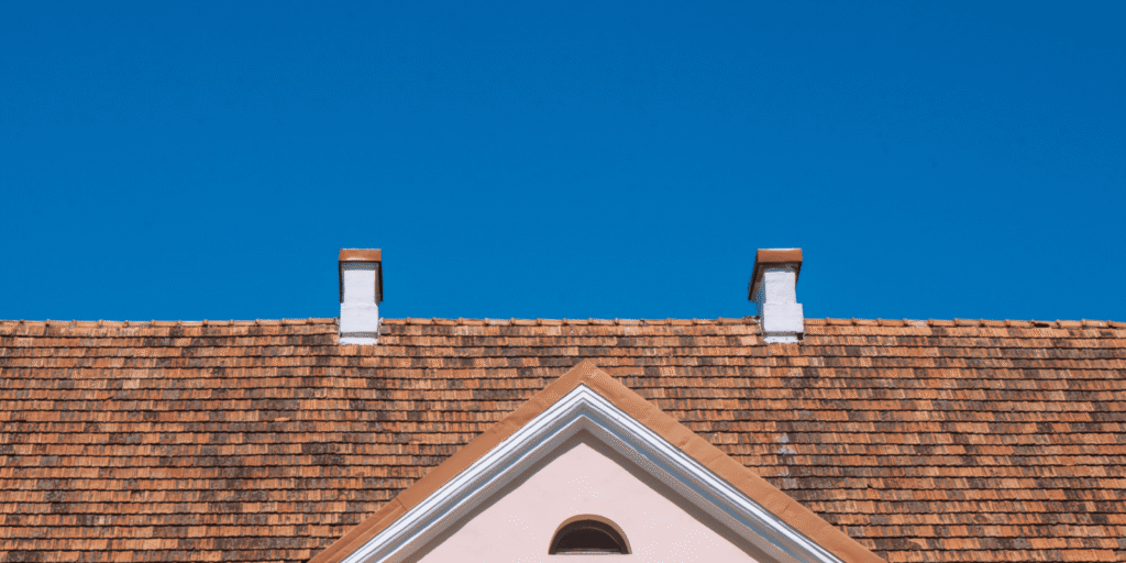 Shingle roof with two chimneys and a gable vent, illustrating how roof design and ventilation can affect attic condensation.