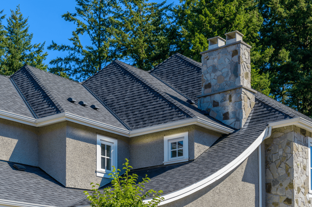 Dark shingle roof with vents and multiple hip sections on a Boston area home where attic insulation gaps trap summer heat