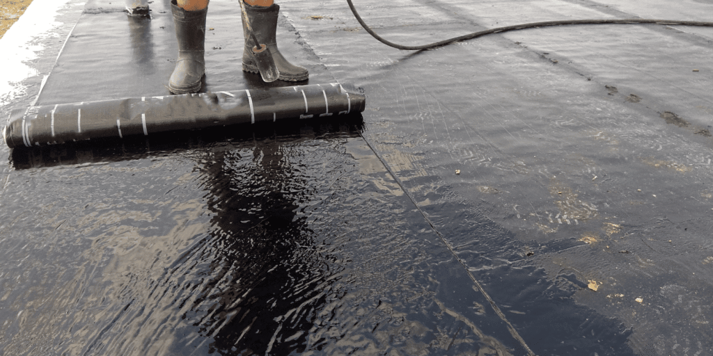 Flat roof membrane with visible water and worker, showing drainage problems that can cause ponding after rain and repairs.