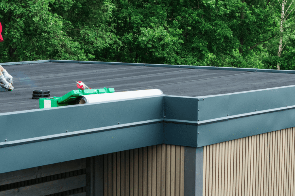 Flat roof worker applying maintenance near a roof drain, showing how flat roof drainage problems should be checked early.