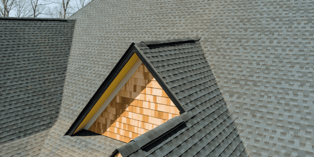 Shingle roof with visible ridge vents and dormers, illustrating ridge vent vs soffit vent airflow across a residential home.