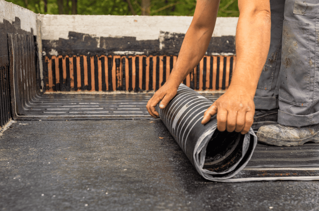 Roofer installing waterproofing membrane on a flat roof, showing roof membrane repair options for damaged areas and seams.
