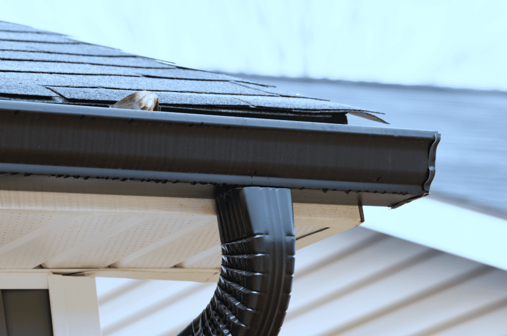 Debris in a gutter and downspout on a shingle roof edge, one of the most common roof downspout problems homeowners face