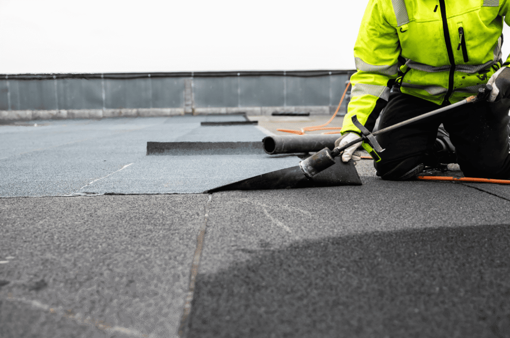 Roofer working on a flat roof membrane near a drain area, sealing the weak points that cause flat roof leaks around drains
