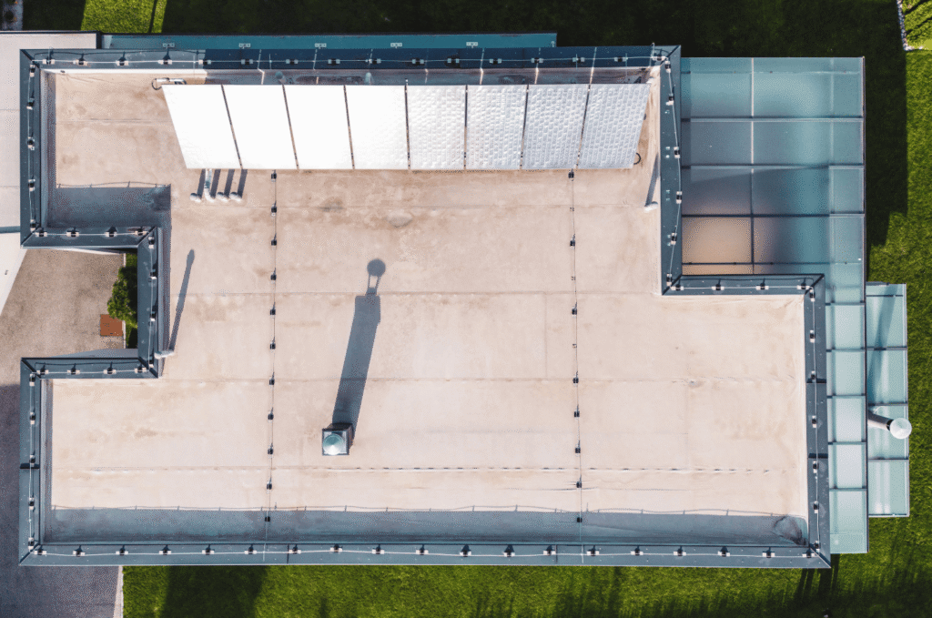 Aerial view of a flat membrane roof showing long seam lines between sheets, a leading cause of flat roof leaks on aging roofs