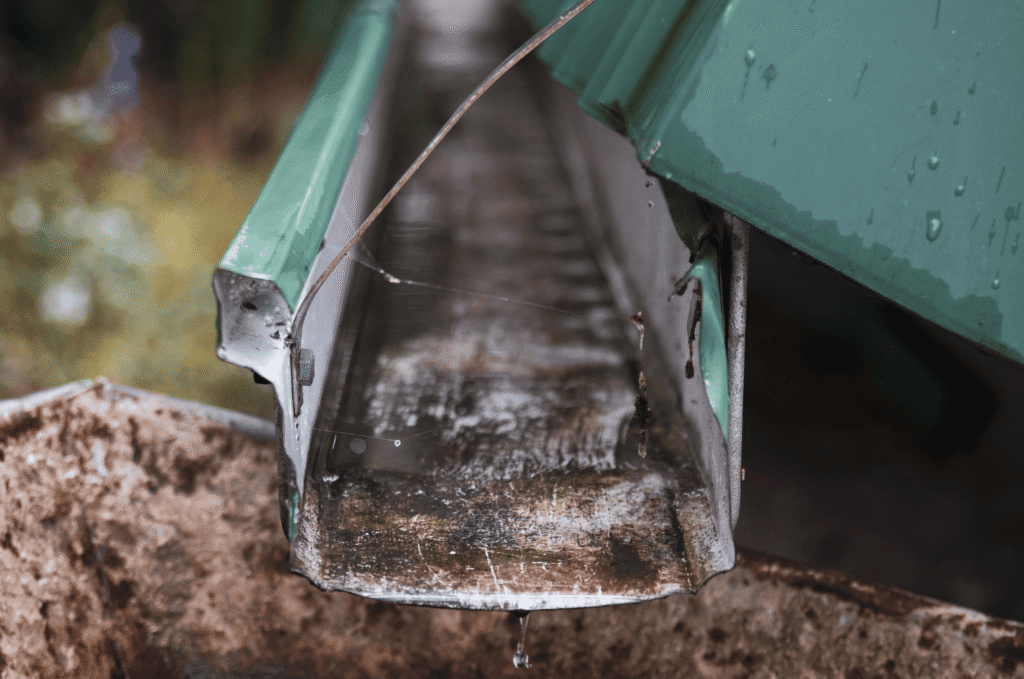 Water dripping from an old gutter into a pool below, showing how roof downspout problems soak the soil and damage foundations