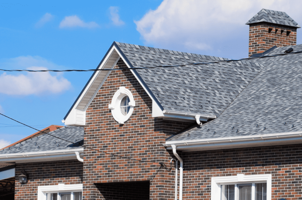 Asphalt shingle roof with chimney and vents after professional roof vent leak repair, sealed and watertight on a brick home